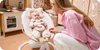 A mother interacting with her baby in a baby bouncer in a nursery. Produktbild-Vorschau