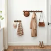 A hallway or entryway with a wooden coat rack mounted on a white wall, displaying coats, hats, and a bag. Produktbild-Vorschau