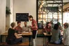 People are dining at tables in a restaurant, with a waiter taking an order. Produktbild-Vorschau