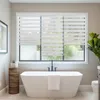 A modern bathroom with a freestanding bathtub and a large window covered by striped blinds. Podgląd zdjęcia produktu
