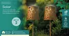 Two solar stake lights with decorative floral patterns are shown in a garden setting. Produktbild-Vorschau
