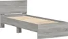 A simple, modern bed frame with a headboard and wooden slats, shown from a side angle against a white background. The frame is a light grey wood-effect material. Voir les images du produit