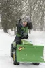 A child is riding a toy tractor with a snow plow attachment in the snow. Produktbild-Vorschau