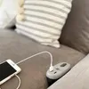 A smartphone is plugged into a charging device on a sofa. Produktbild-Vorschau