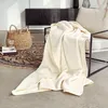 A cream-colored blanket draped over a chair next to a basket and books. Produktbild-Vorschau