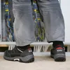 A person wearing work pants and safety shoes stands in front of an electrical panel. Produktbild-Vorschau
