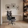 A black ergonomic office chair with a footrest is placed in a home office setting next to a desk and a bookshelf. Produktbild-Vorschau