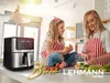 A mother and daughter are in a kitchen, preparing food. An air fryer is prominently displayed on the counter. Voir les images du produit
