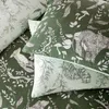A close-up view of green bedding with a forest-themed print featuring animals and foliage. Voir les images du produit