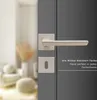 A close-up of a door handle and lock mechanism on a gray door, with a blurred interior scene in the background. Produktbild-Vorschau