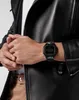 A person wearing a black leather jacket and a watch on their wrist. Produktbild-Vorschau