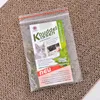 A clear plastic bag containing catnip and a product label, resting on a cardboard scratching surface. Produktbild-Vorschau