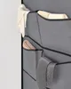 A close-up of a gray fabric storage organizer hanging on a white wall. It contains rolled-up items and folded accessories like gloves, a scarf, and ties. Náhled obrázku produktu