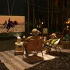 Two people are watching a movie projected outdoors at night in a forest setting. Produktbild-Vorschau