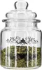A clear glass jar filled with dried green tea leaves, featuring decorative black floral accents and the word "TEA" printed on the front. Produktbild-Vorschau