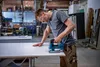 A man is using a jigsaw to cut a piece of material in a workshop. Anteprima dell’immagine prodotto