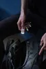 A person is holding a small flashlight attached to keys and shining it into an open backpack. Anteprima dell’immagine prodotto