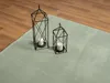 Two black geometric lanterns with white candles sit on a light green rug next to a wooden floor. Produktbild-Vorschau