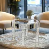 A mirrored round coffee table with books and a decorative plant sits on a fluffy white rug in a living room setting with two chairs. Anteprima dell’immagine prodotto