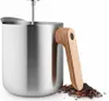 A stainless steel teapot with a wooden handle and a pile of loose tea leaves next to it. Náhled obrázku produktu