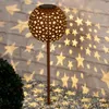 A solar-powered garden light with a star pattern is illuminating a brick wall and the ground with star-shaped light projections. Produktbild-Vorschau