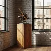 A rustic wooden pedestal with a metal and wood sculpture on top, placed near a window in a brick-walled room. Voir les images du produit