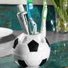 A soccer ball-shaped toothbrush holder with toothbrushes and toothpaste inside, placed on a countertop. Produktbild-Vorschau