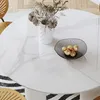 A close-up view of a round white dining table with marble-like veining, featuring a vase of dried flowers and a bowl of decorative orbs. Produktbild-Vorschau