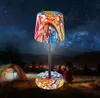A graffiti-style LED table lamp is set up outdoors at night, with a tent and people in the background. Anteprima dell’immagine prodotto