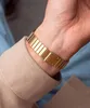 A close-up shot of a person's wrist wearing a gold-colored watch. Voir les images du produit