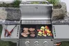 A gas grill with food cooking on it, set up outdoors. Náhled obrázku produktu