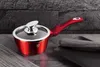 A red pot with a glass lid and a red handle sits on a dark countertop, with a dark gray napkin and a black plate to the right. The background is a dark gray textured wall. Anteprima dell’immagine prodotto