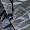A close-up of a black drawstring with a plastic toggle on a gray, textured fabric. Náhľad obrázku produktu