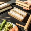 A person's hand is shown holding a bamboo sushi rolling mold over a sushi making kit with rice, chopsticks, and ingredients. Náhľad obrázku produktu