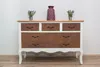 A dresser with a wood top and white frame, featuring drawers with a rust-like pattern, decorated with two small potted plants and a vase. Náhľad obrázku produktu