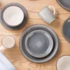A top-down view of a set of ceramic dishes and mugs arranged on a wooden surface. Produktbild-Vorschau