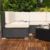 A close-up view of a black rattan outdoor sofa set with beige cushions, placed on a wooden deck, with green foliage in the background. Anteprima dell’immagine prodotto