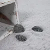Three small, dark, textured objects resembling stones are scattered on a soft, light gray, fluffy surface. A distressed, white wooden object is partially visible in the upper left corner. Produktbild-Vorschau