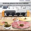 A raclette grill with various food items like cheese, salami, pickles, and bread laid out in front of it. Produktbild-Vorschau