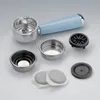 A collection of espresso machine accessories, including a portafilter, filter baskets, and coffee pods, laid out on a light gray surface. Podgląd zdjęcia produktu