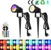 Two black LED garden spotlights with ground stakes, one displaying a rainbow of colors and the other a warm white light, are shown alongside a remote control and examples of different light colors. Anteprima dell’immagine prodotto