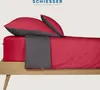 A bed with red and gray bedding, including pillows and a fitted sheet. Produktbild-Vorschau