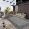 An outdoor patio or balcony with a rug, seating, and plants. Podgląd zdjęcia produktu