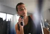 A man is shaving his face with an electric shaver in a bathroom. Podgląd zdjęcia produktu