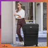A woman leans against a wall next to a black suitcase. Anteprima dell’immagine prodotto