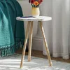 A small round side table with a vase of flowers and a phone on it, next to a teal blanket and white curtains. Produktbild-Vorschau