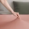A hand is shown stretching a peach-colored fabric, likely a bedsheet, against a background of pillows. Produktbild-Vorschau