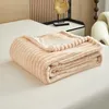 A folded beige plush blanket is placed on a bed. Produktbild-Vorschau