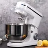 A white stand mixer with a stainless steel bowl is shown against a textured gray background. Two lemon halves are visible in the foreground. Produktbild-Vorschau
