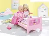Two dolls are sitting on a pink doll bed, reading a book. Produktbild-Vorschau